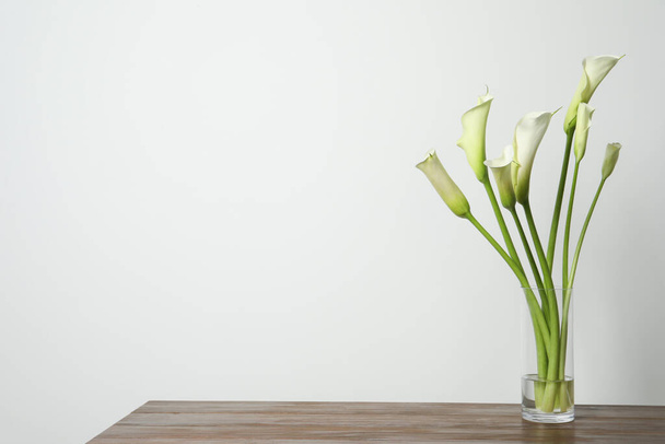 Beautiful calla lily flowers in vase on wooden table against white background. Space for text - Fotoğraf, Görsel