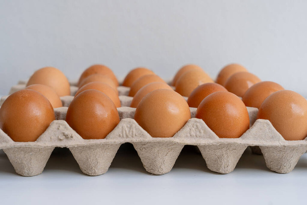 Huevos de pollo crudos en una bandeja de cartón, fondo de huevos marrones de granja. - Foto, imagen