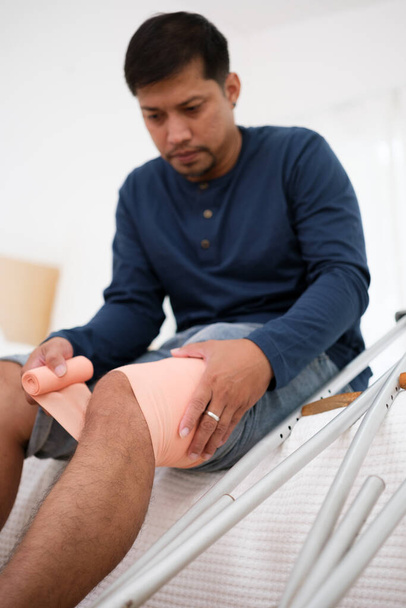 Азиатский человек использует костыли, потому что он infury на колене, и он первая помощь с бинтом. - Фото, изображение