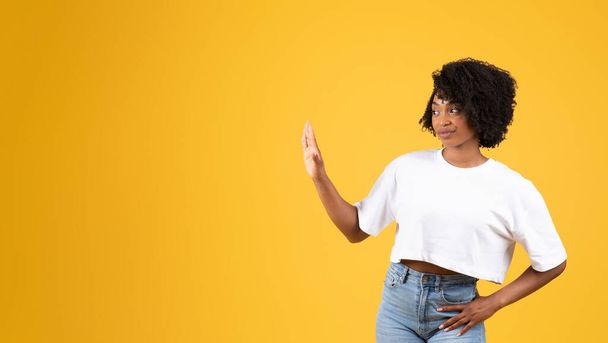 Mujer negra milenaria insatisfecha en gesto casual haciendo stop con la mano, aislada sobre fondo de estudio naranja, panorama. Espacio personal, emociones humanas, estilo de vida y decir no - Foto, imagen