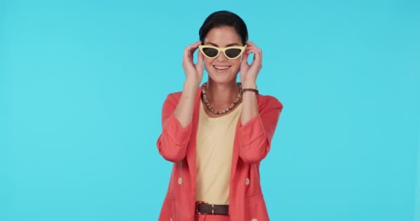 Sunglasses, fashion and wink with a model woman in studio on a blue background for trendy style. Portrait, shades and smile with a happy young female person looking playful while flirting in clothes. - Footage, Video