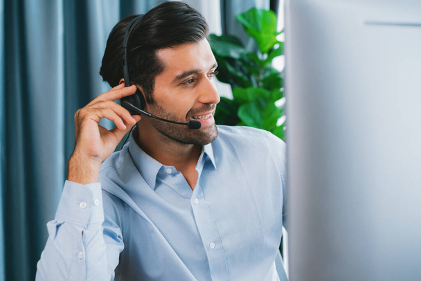 Male call center operator or telesales representative siting at his office desk wearing headset and engaged in conversation with client providing customer service support or making a sale. fervent - Foto, immagini