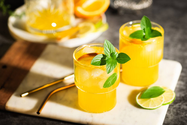 Lemonade or mojito cocktail with fruits and basil. Lemon and orange cold summer drink on grey table - Foto, Bild