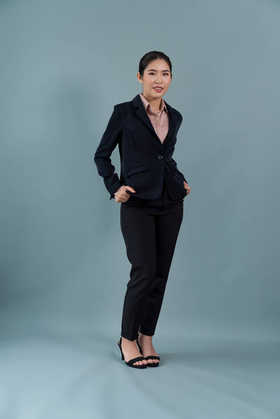 Full body length image of confident young businesswoman stands on isolated background, posing in formal black suit. Office lady or manager with smart and professional appearance. Enthusiastic - Photo, image