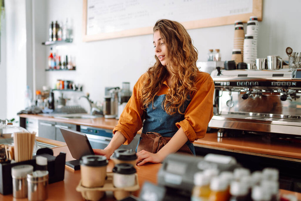 Beautiful woman owner stands behind the counter of a coffee shop. A barista with a digital tablet takes an order. Business concept. Takeaway food. - Photo, image