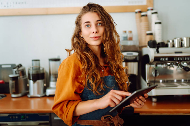 Beautiful woman owner stands behind the counter of a coffee shop. A barista with a digital tablet takes an order. Business concept. Takeaway food. - Foto, Imagem