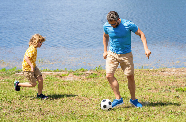 dad and son playing football during their childhood. Childhood memories of son and his dad. dad have fun with his son. journey of fatherhood. dad and son enjoying childhood adventures outdoor. - Фото, изображение