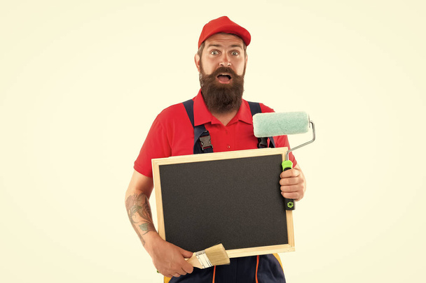 amazed man painter with blackboard in renovation studio. man painter ready for renovation isolated on white background. man painter advertising renovation. man painter offer renovation. - Fotó, kép
