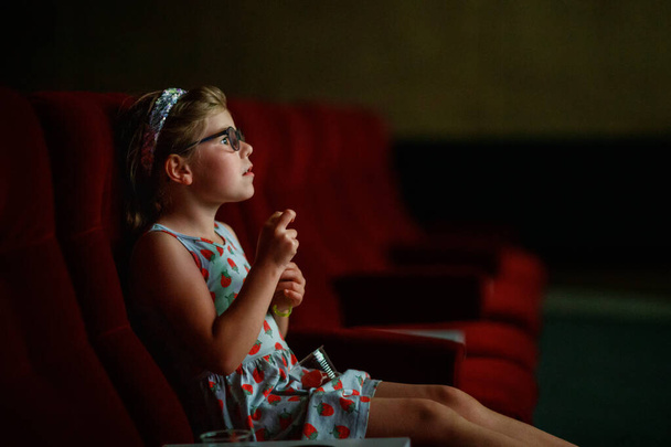 Маленька дівчинка дошкільного віку в окулярах дивиться мультфільм або фільм у кіно. Щаслива дитина. Сімейна діяльність з дітьми - Фото, зображення