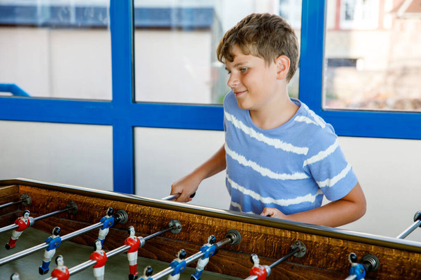 Smiling school boy playing table soccer. Happy excited child having fun with family game with siblings or friends. Positive kid - Fotografie, Obrázek