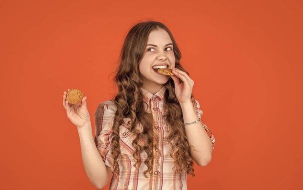 hungry teen girl with oatmeal cookies on orange background. - Foto, Imagen