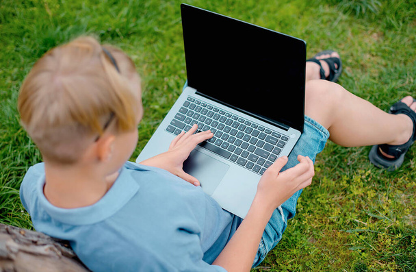 młody chłopiec na trawie w parku lub ogrodzie przy użyciu laptopa - Zdjęcie, obraz