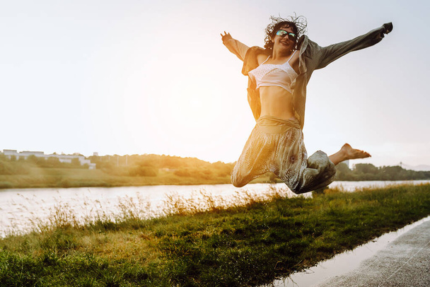 Портрет Щасливий танцюючий босоніж в калюжах, дівчина-підліток, з мокрим волоссям, у вільному літньому одязі, на заході сонця, після дощу, біля річки. концепція насолоди природою, заходу сонця, свободи, - Фото, зображення