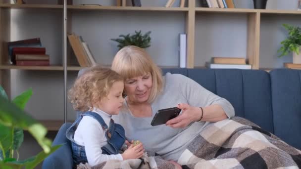 Grandmother and granddaughter use a smartphone, they have fun together. - Materiał filmowy, wideo