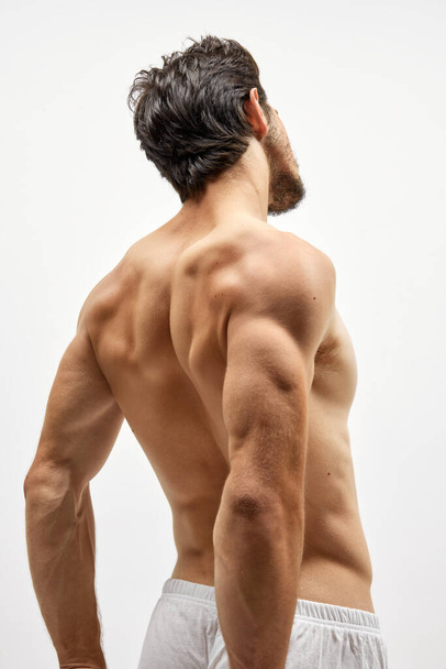 Strength, power and beauty. Back view of strong musculed young man posing topless over white background. Beauty, fashion, sport, fitness and body care concept - Zdjęcie, obraz