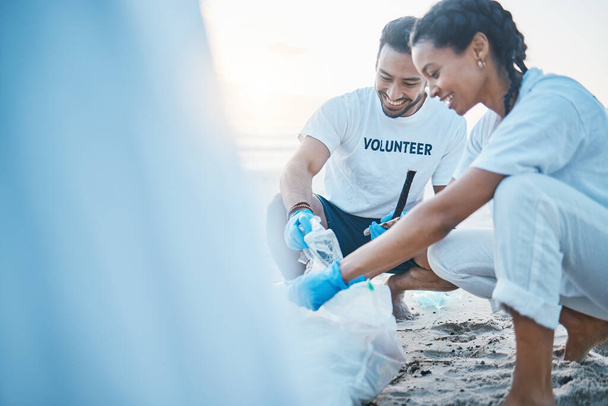 Vrijwilliger, model en mensen schoonmaken strand voor de wereld aarde dag, zorg en vriendelijkheid voor de natuurlijke omgeving. Helpen, recyclen en gelukkig man en vrouw oppakken van plastic afval en vervuiling op oceaan zand - Foto, afbeelding