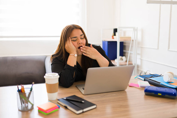 Уставшая деловая женщина с большим количеством работы зевает и чувствует сонливость и усталость во время работы в офисе - Фото, изображение