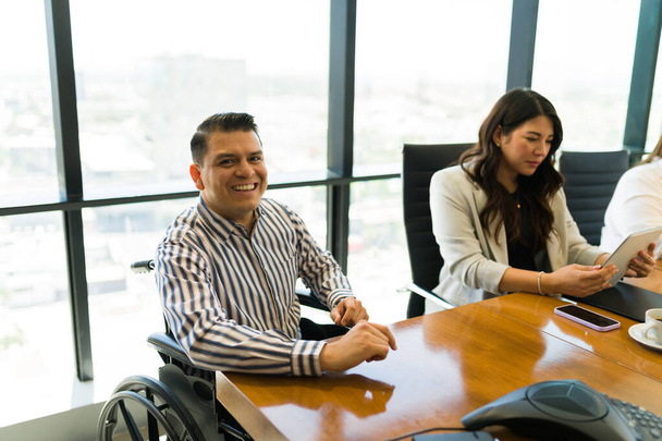 Feliz hombre de negocios adulto medio sentado en una silla de ruedas con colegas sentados en la sala de reuniones de la oficina - Foto, Imagen