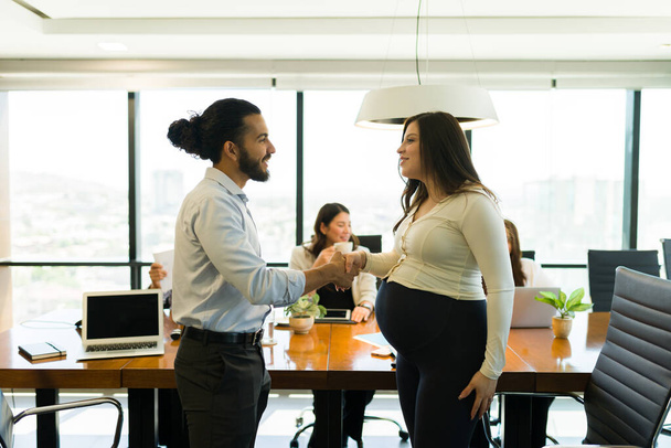 Бизнесмен пожимает руку беременной коллеге во время встречи в офисном зале - Фото, изображение
