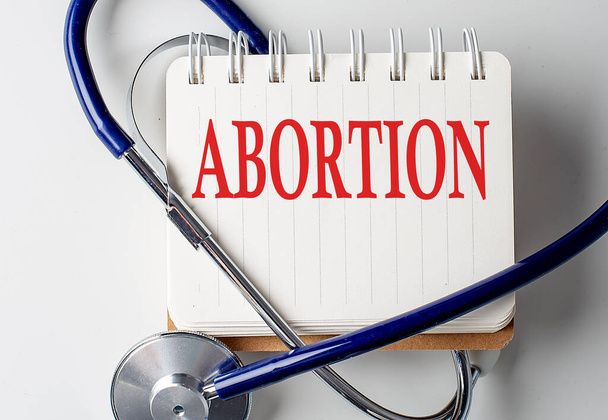 ABORCIÓN palabra en el cuaderno con equipo médico en un segundo plano - Foto, imagen