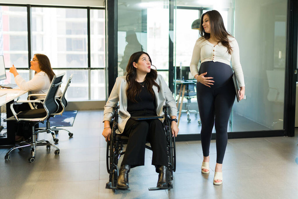 現代のオフィスで妊娠中の同僚と話し合う車椅子障害者のビジネス女性 - 写真・画像