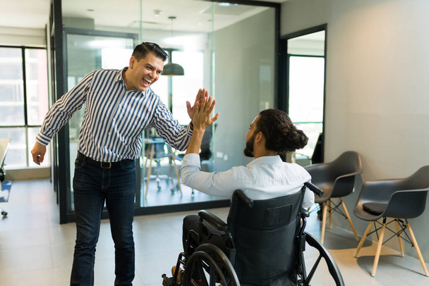 Веселий середній дорослий бізнесмен дає п'ять інвалідів колезі на інвалідному візку в офісі - Фото, зображення