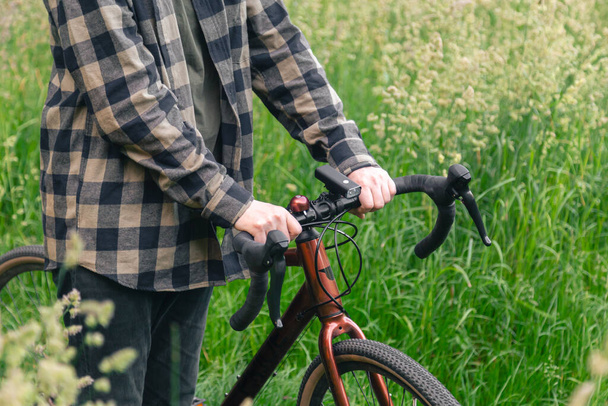 Um homem segura o volante de uma bicicleta e caminha na floresta entre a grama verde, close-up. - Foto, Imagem