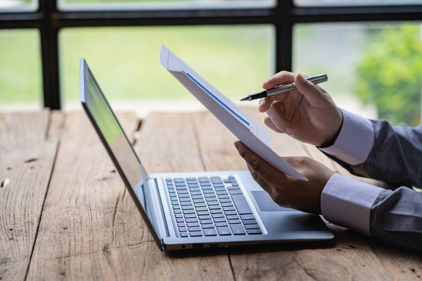 Jovem analista de mercado financeiro trabalhando no escritório com laptop enquanto sentado à mesa de madeira Empresário analisando documentos em sua mesa imagens de close-up - Foto, Imagem