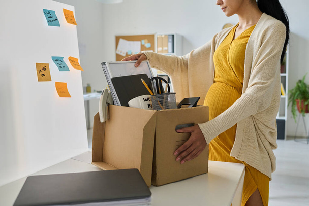 Young pregnant businesswoman packing her things in box, she going on maternity leave - Foto, Imagem