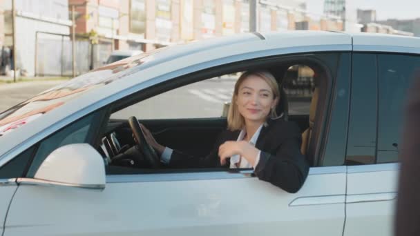 Kaukázusi fiatal nő öltönyben elviszi a kulcsokat álmai kocsijából. Kellemes szőke nő ül a vezetőülésen és mosolyog a kamera előtt. Vásárlási és szállítási koncepció. Kulcsok az új álomautójából.. - Felvétel, videó