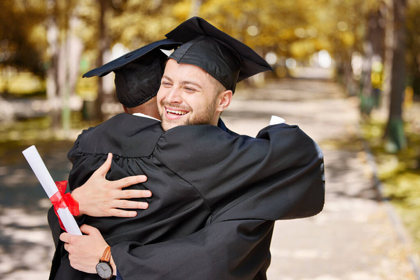 University graduation, happy man and friends hug for success of college achievement, winning or motivation outdoor. Excited male students embrace to celebrate dream, graduate goals or education award. - Фото, изображение
