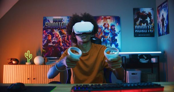 El jugador adolescente con auriculares VR juega un videojuego virtual en línea usando controladores inalámbricos. chico afroamericano divirtiéndose en el tiempo libre en su habitación. Juegos en casa. Vista desde la perspectiva de la pantalla del PC. - Foto, imagen