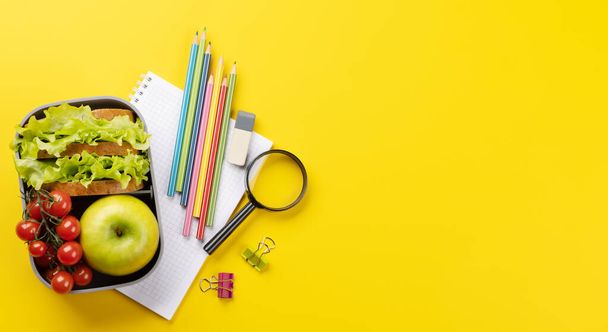 School supplies, stationery, and lunch box on yellow background. Education and nutrition. Flat lay with blank space - Photo, Image