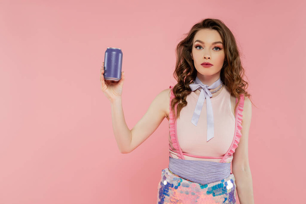 pop concept, aantrekkelijke jonge vrouw met golvend haar holding soda blik met koolzuurhoudende drank, reclame, staan op roze achtergrond, mode model in stijlvolle outfit, vrouwelijkheid, pop pose  - Foto, afbeelding