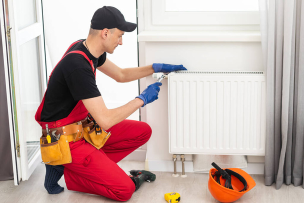 Centrale verwarming monteur en klusjesman repareren van huis radiator, gas crisis en seizoensgebonden problemen. Hoge kwaliteit foto - Foto, afbeelding