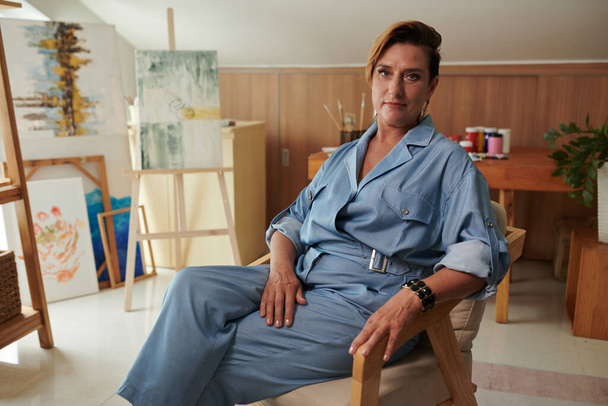 Portrait of elegant mature woman leaning back in her chair when resting in studio after painting - Photo, Image