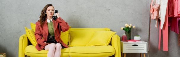 telefoongesprek, aantrekkelijke vrouw met golvend haar zittend op de gele bank, huisvrouw pratend op retro telefoon, poserend als een pop, wegkijkend, modern interieur, woonkamer, banner  - Foto, afbeelding