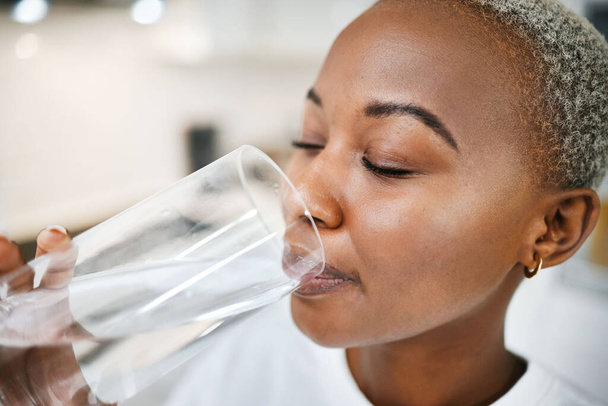 Wellness, szkło i kobieta piją wodę dla zdrowia, nawilżenia i płynnego odżywiania w swoim domu. Spragniona, energiczna i afrykańska kobieta ciesząca się zimnym zdrowym napojem w kuchni swojego mieszkania - Zdjęcie, obraz