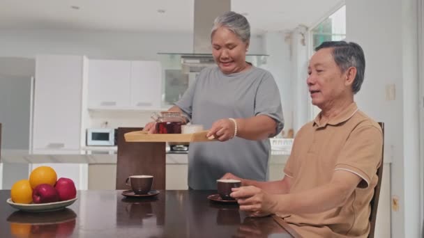 Średnie ujęcie starszej kobiety nalewającej herbatę do kubka męża przy śniadaniu - Materiał filmowy, wideo