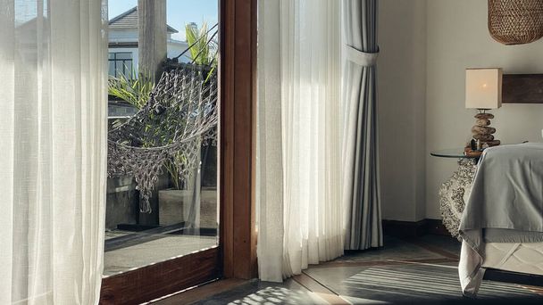 Comfortable boho style grey macrame hammock and palm houseplants on balcony. View from room. - Fotoğraf, Görsel