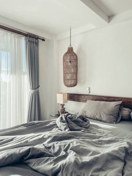 Dormitorio estilo loft con juego de ropa de cama gris, lámparas de mimbre colgantes y mesita de noche - Foto, Imagen