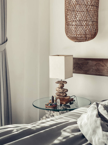 Bedside table with night light, different healing crystals and wicker hanging lamp in the bedroom - Zdjęcie, obraz
