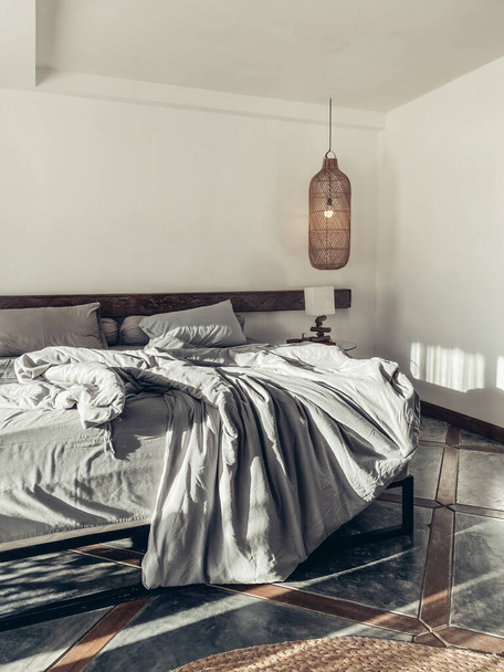 Loft style bedroom with gray bed linen set, hanging wicker lamps and bedside table - Fotografie, Obrázek