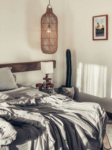 Loft style bedroom with gray bed linen set, hanging wicker lamps and bedside table. The photo in the frame was taken by me. - Photo, image
