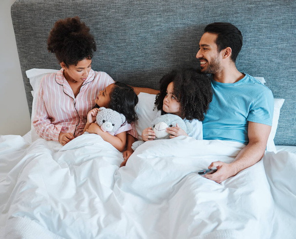 Bonding, discussion and children in the bed with their parents talking and relaxing together in the room. Happy, smile and girl kids speaking for conversation with their mother and father in bedroom - 写真・画像