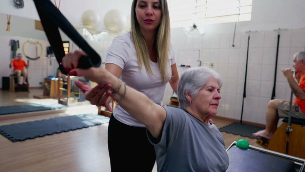 Instruktorka Pilates trenuje starszą białą kobietę do ćwiczeń w sesji rehabilitacji fizjoterapii - Zdjęcie, obraz