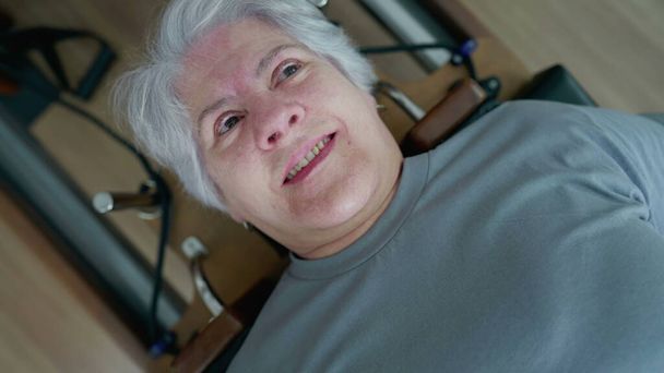 Közelkép a Senior Woman 's Face Pilates gépi gyakorlat során, részt vesz a gerinc egészségügyi edzés rutin - Fotó, kép