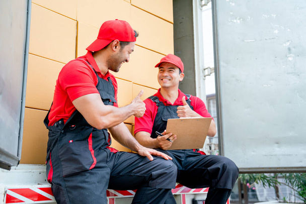 Two delivery men sit and discuss together also show thumbs up on back part of truck during move package or boxes to customer house. - Foto, imagen
