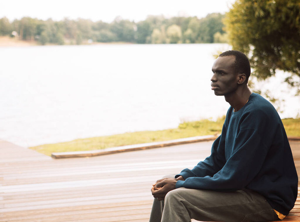 A young black man sitting on bench near lake . Summer day. Lifestyle concept. - Foto, Imagem