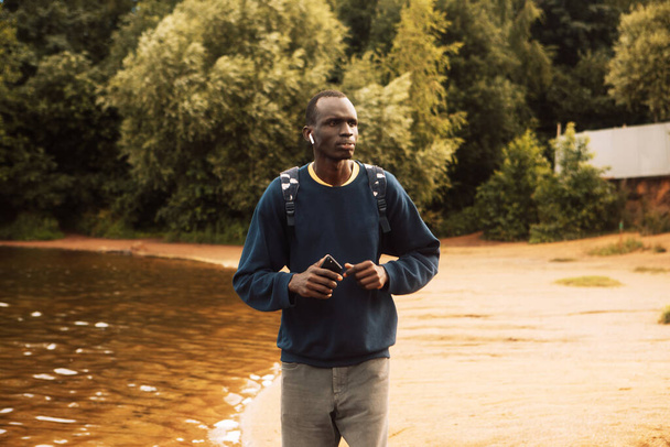 A young black man jogging near a lake with headohones. Morning. Summer day. Lifestyle and sport concept. - Foto, Bild